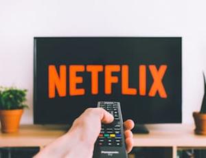 Ein Mensch schaltet mit Fernbedienung den Pay-per-use-Dienst Netflix ein. © freestocksorg