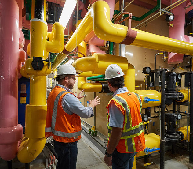 Two workers inside the water treatment plant. Yellow and pink pipes.